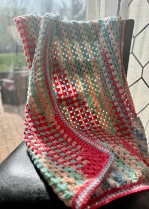 multi-colored crochet baby blanket hung over chair