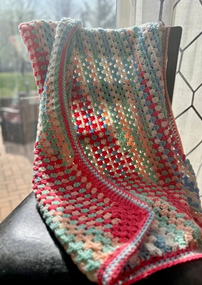 multi-colored crochet baby blanket hung over chair