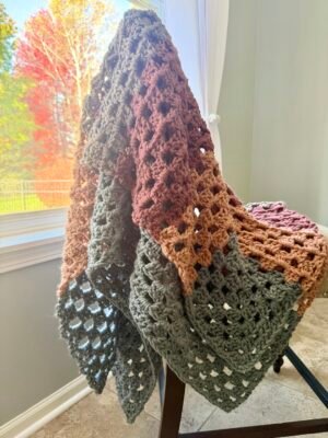 chunky crochet blanket hanging on chair in earthy colors