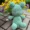 green frog crochet plushie sitting by yellow and purple flowers
