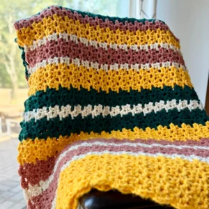 chunky crochet blanket in yellow, green and rose stripes hung over chair